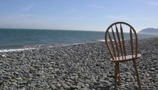 Old wooden chair on a pebbled beach.