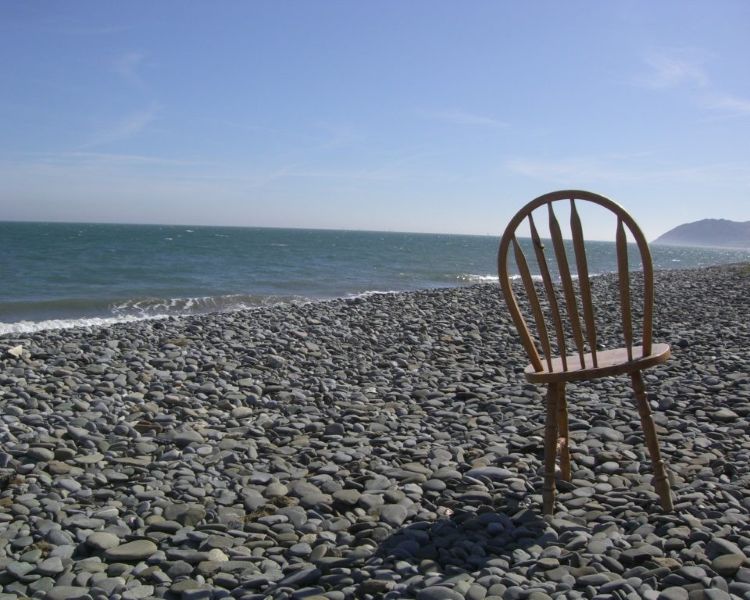Old wooden chair on a pebbled beach.