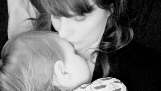Black and white close-up of a mom kissing her baby on the forehead.