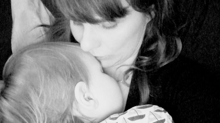 Black and white close-up of a mom kissing her baby on the forehead.
