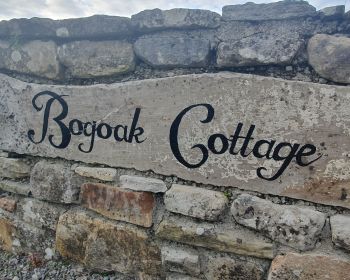 Sign for Bogoak Cottage on a stone wall in the Irish countryside.